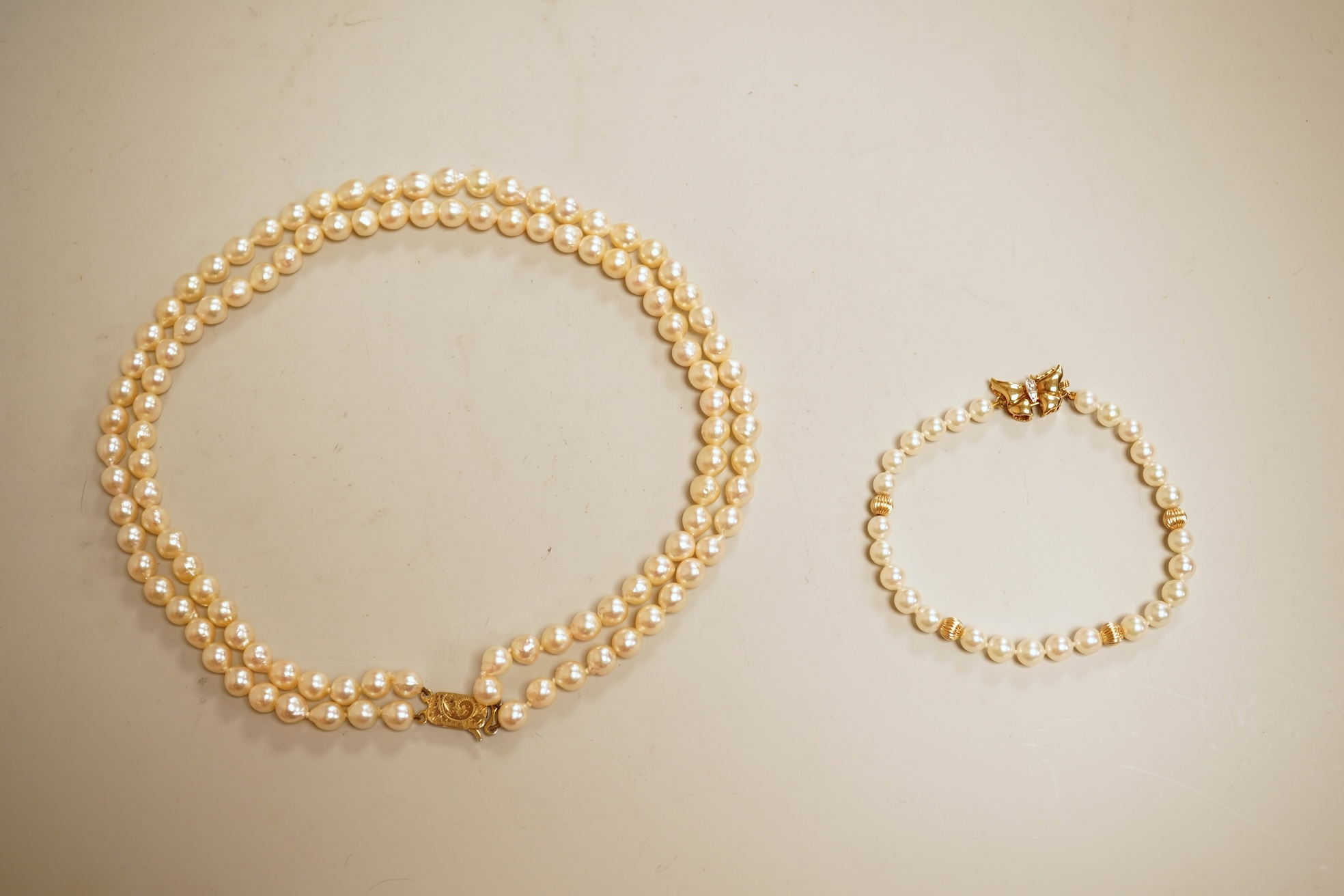 A modern twin strand cultured pearl choker necklace, with an engraved 9ct clasp, approx. 40cm, together with a cultured pearl bracelet, with diamond chip set butterfly shaped 14k clasp, 18cm, with four fluted yellow meta